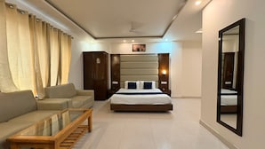 Una habitación de hotel con cama, sofá, mesa de centro de madera, armario y espejo.