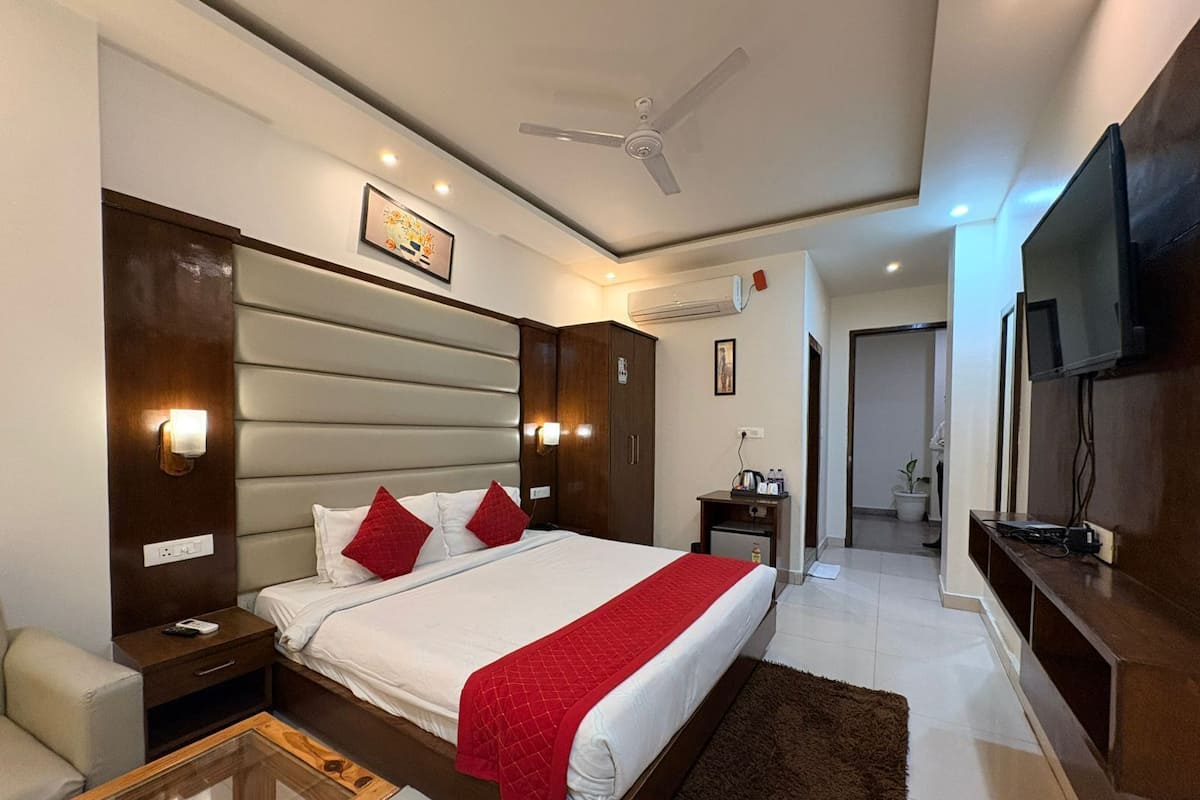 A hotel room with a bed, bedside tables, a TV, a ceiling fan, and a small desk with a chair.