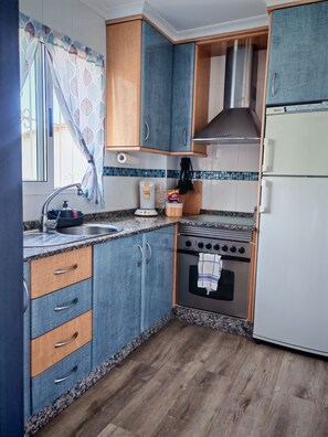 A kitchen with wooden cabinets, a stove, a sink, and a refrigerator. - Costamar, bungalow familiar con terrazas y piscina a 5 minutos de la playa (Los Arenales del Sol)