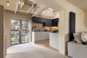 A modern kitchen with a central island, a dining area with a sofa, and a view through a window with a metal gate. - Church Alley House (Cheltenham)