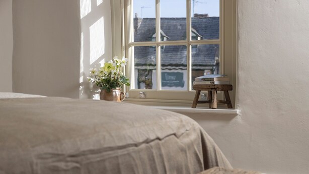 Un dormitorio con una cama, una ventana, una mesita pequeña y una planta en maceta.