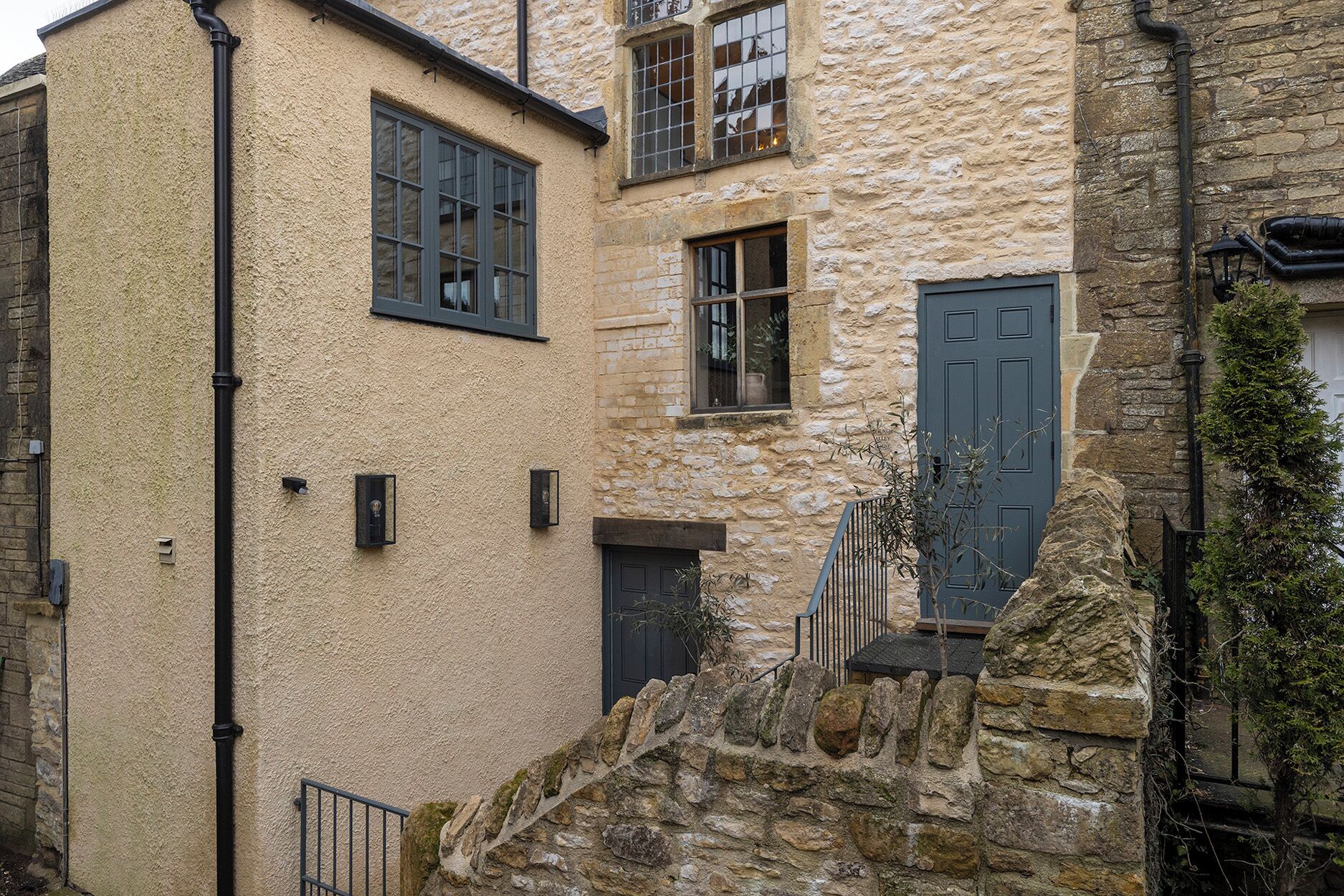 A stone building with a small staircase leading to a door, a window with a grid pattern, and a black pipe running vertically.