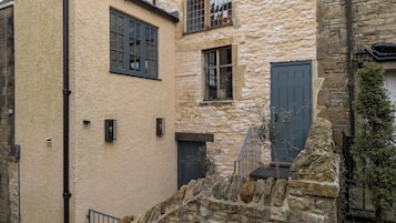 A stone building with a small staircase leading to a door, a window with a grid pattern, and a black pipe running vertically.