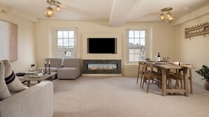 Una sala de estar con chimenea, televisor montado en la pared y comedor con muebles de madera.