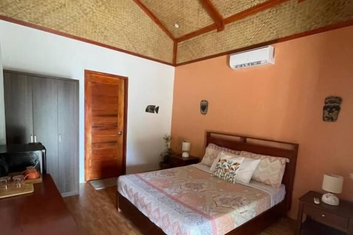 A bedroom with a wooden bed, a wooden table, a ceiling fan, and a small window.