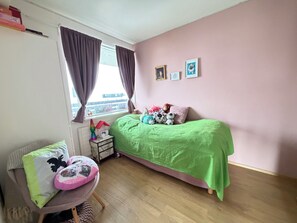 A bedroom with a green bed, a chair with a cushion, a radiator, and a window with curtains. - Modern apartment centrally located in Reykjavik (Reykjavík)