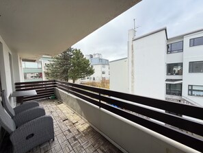 A balcony with a wicker sofa, a small table, and a view of neighboring buildings and a tree. - Modern apartment centrally located in Reykjavik (Reykjavík)