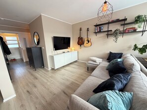 Ein Wohnzimmer mit einer Couch, einem Fernseher, einer Kommode und Gitarren an der Wand.