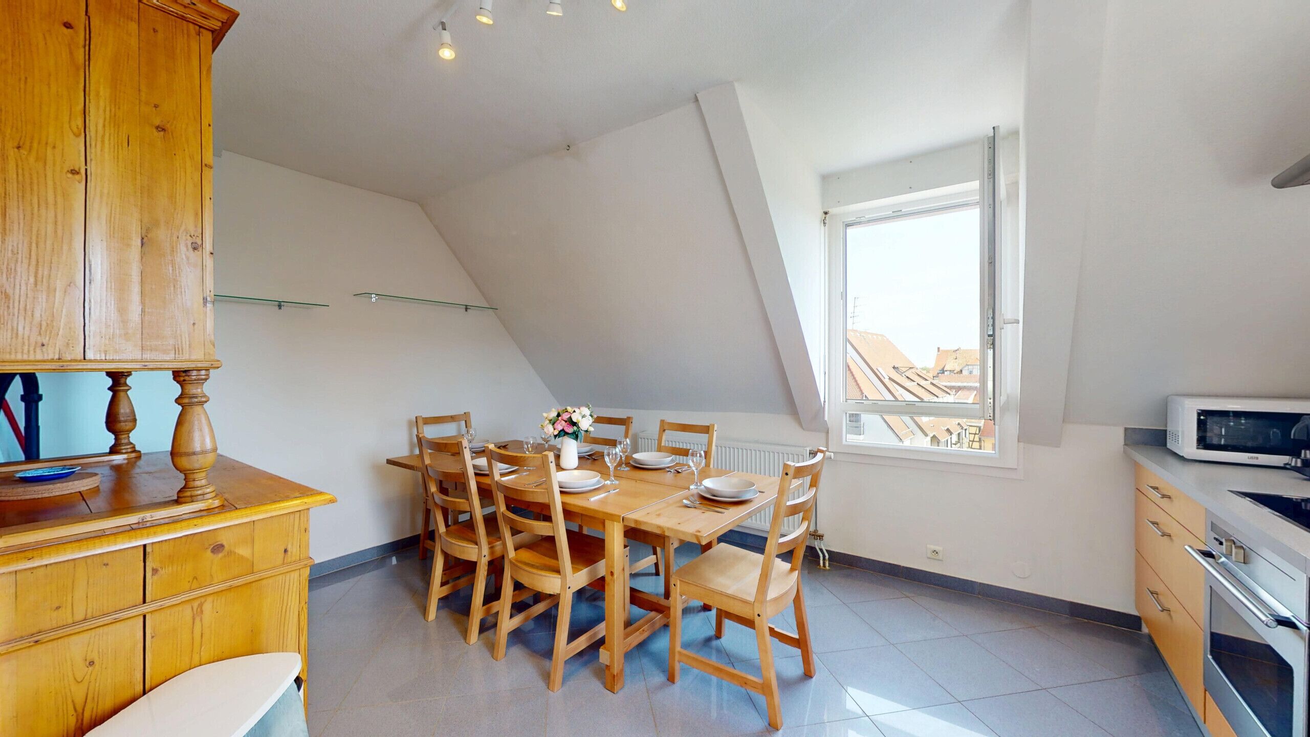 A dining area with a wooden table and chairs, a white cabinet, and a window with a view of buildings.