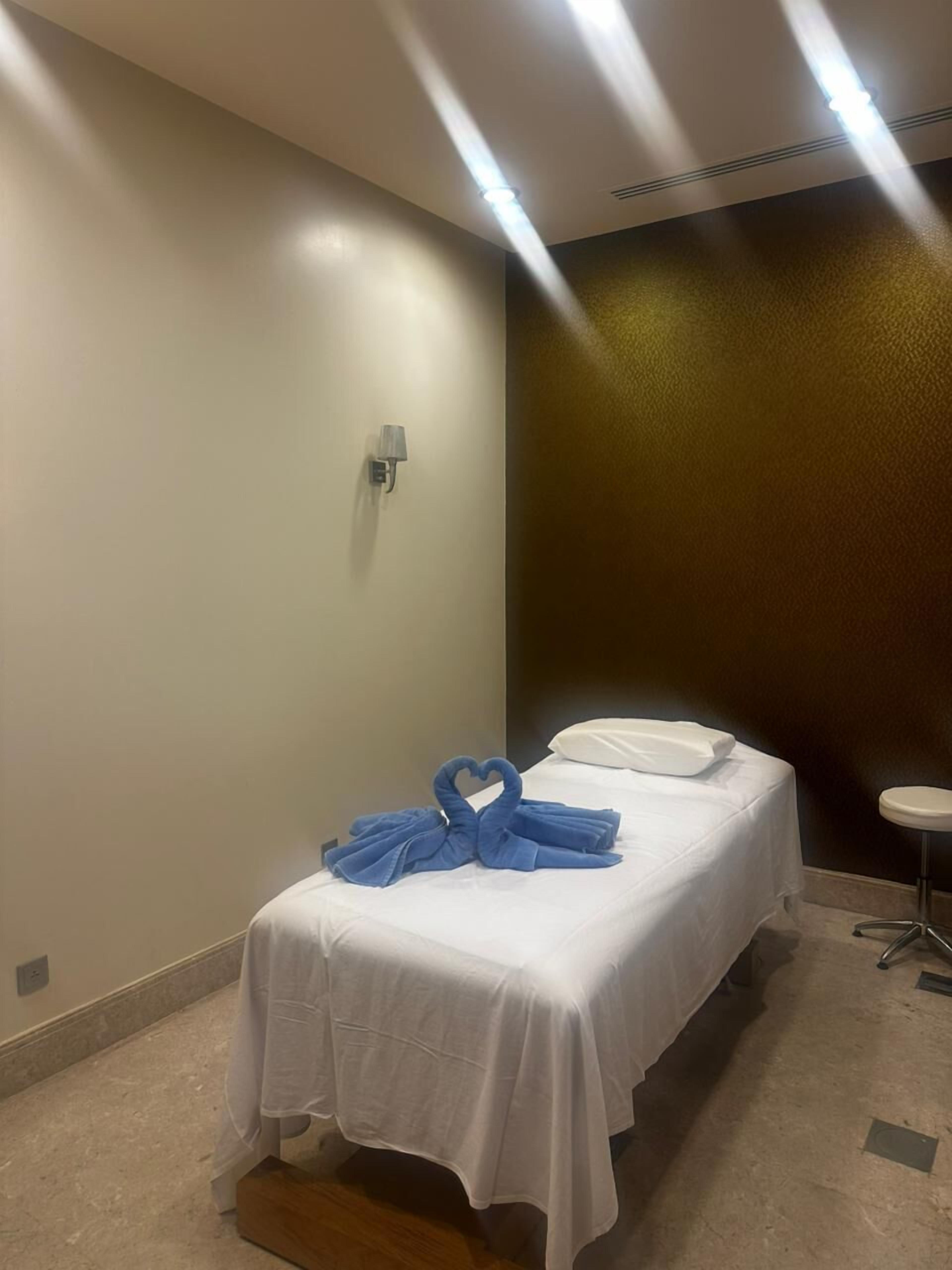 A hotel room with a bed, a wall-mounted lamp, and a small stool.