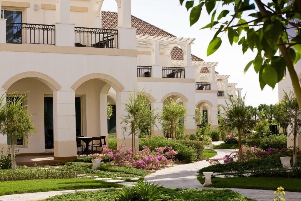 A building with multiple balconies, a garden with various plants, and a pathway leading to the entrance.