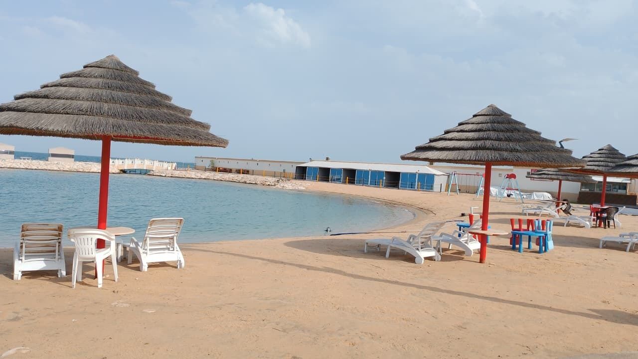 A beach with thatched umbrellas, lounge chairs, and a poolside area.