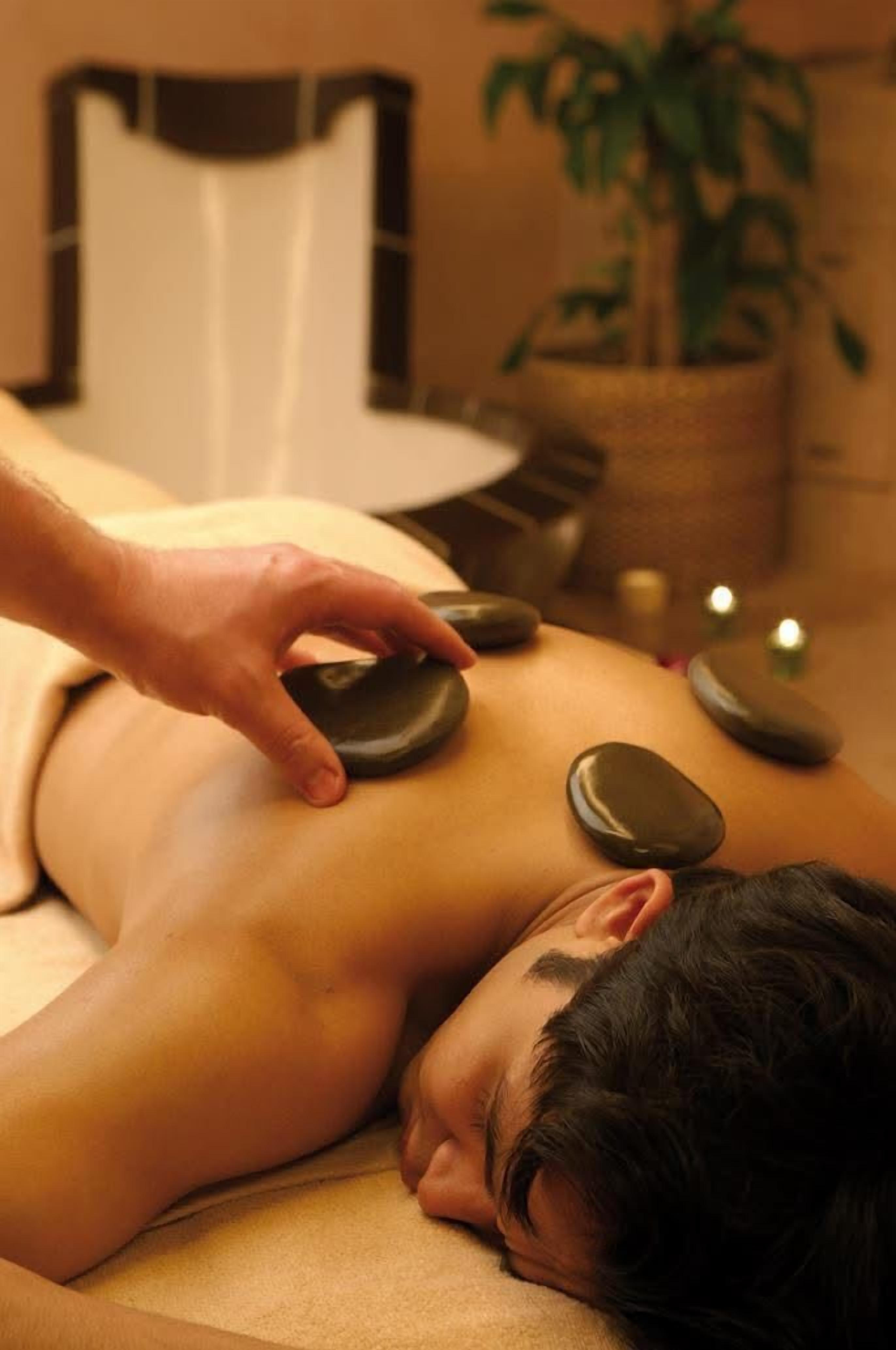 A person receiving a stone massage on a massage table in a room with a chair and a potted plant.