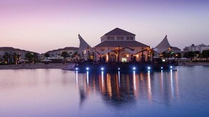 A waterfront hotel with a central building, multiple umbrellas, and a calm water body reflecting the lights. - Move on Beach Resort Al Khobar (Al Khobar)