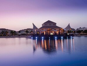 A waterfront hotel with a central building, multiple umbrellas, and a calm water body reflecting the lights. - Move on Beach Resort Al Khobar (Al Khobar)