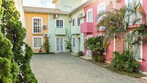 A courtyard with cobblestone pavement, surrounded by buildings with pastel-colored facades and air conditioning units. - Mariscal Ideal Family Retreat, King Bed, Complete Linens, 220m from the Sea (Bombinhas)
