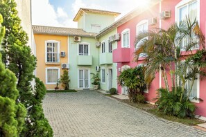A courtyard with cobblestone pavement, surrounded by buildings with pastel-colored facades and air conditioning units. - Your home in Mariscal: Air conditioning and king-size bed 220m from the sea. (Bombinhas)