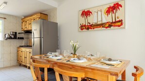 A kitchen with a refrigerator, wooden cabinets, and a dining table set for four with chairs. - Mariscal Ideal Family Retreat, King Bed, Complete Linens, 220m from the Sea (Bombinhas)