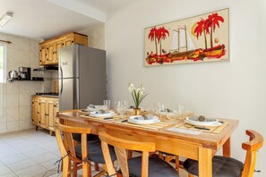 A kitchen with a refrigerator, wooden cabinets, and a dining table set for four with chairs. - Your home in Mariscal: Air conditioning and king-size bed 220m from the sea. (Bombinhas)