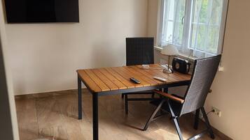 Une pièce avec une table en bois, une chaise noire, un téléviseur fixé au mur et une fenêtre avec des rideaux.