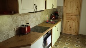 A kitchen with white cabinets, a wooden countertop, a red kettle, a coffee maker, and patterned floor tiles. - Bungalow with lake view & fenced garden - quiet & private (Rüdersdorf bei Berlin)