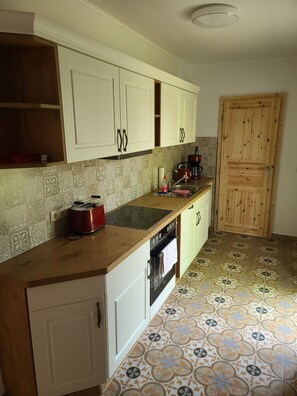 A kitchen with white cabinets, a wooden countertop, a red kettle, a coffee maker, and patterned floor tiles. - Bungalow with lake view & fenced garden - quiet & private (Rüdersdorf bei Berlin)