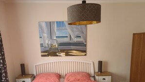 A bedroom with a bed, a nightstand, a lamp, a painting, and a wardrobe. - Bungalow with lake view & fenced garden - quiet & private (Rüdersdorf bei Berlin)