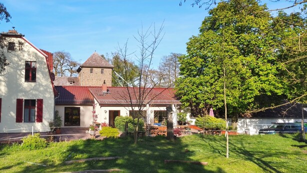 A two-story house with a red roof, a tower, and a garden with potted plants. - Bungalow with lake view & fenced garden - quiet & private (Rüdersdorf bei Berlin)