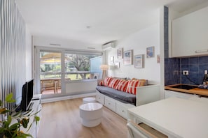 Een moderne woonkamer met een bank, een flatscreen-televisie, een eettafel en een keuken met een blauwe achterwand.