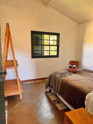 A bedroom with a wooden ladder, a bed with a brown blanket, a window with a black frame, and a patterned rug.