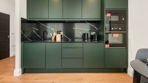 Una cocina moderna con armarios verde oscuro, encimera negra y horno empotrado.