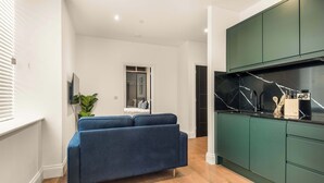 Una sala de estar moderna con un sofá, un televisor y una cocina con armarios verdes.