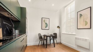 Una cocina moderna con encimera negra, armarios verdes y un comedor con una mesa redonda y dos sillas.