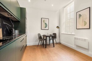 Eine moderne Küche mit schwarzem Arbeitsplatz, grünen Schränken und einem Essbereich mit rundem Tisch und zwei Stühlen.