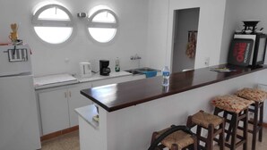 Une cuisine avec deux fenêtres rondes, une machine à café, une bouteille d’eau et un coin bar avec des tabourets.