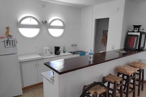 A kitchen with two round windows, a coffee maker, a water bottle, and a bar area with stools. - Fantástica casa a primera linea del mar en empuriabrava (Empuriabrava)