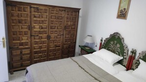Une chambre avec une armoire en bois, un lit avec une tête de lit verte, une table de chevet avec une lampe et un tableau encadré au mur.