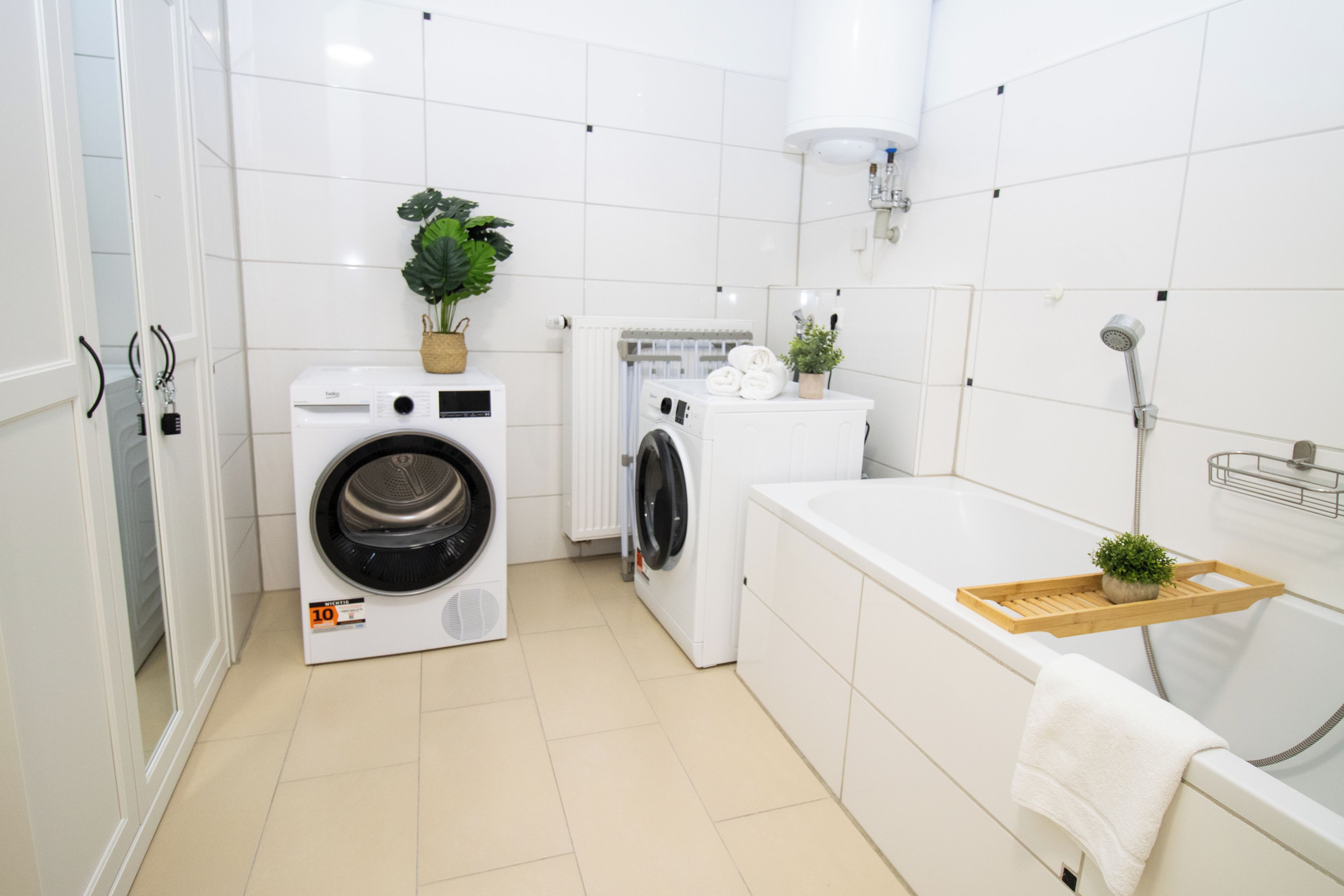 A modern bathroom with a washing machine, dryer, and bathtub.