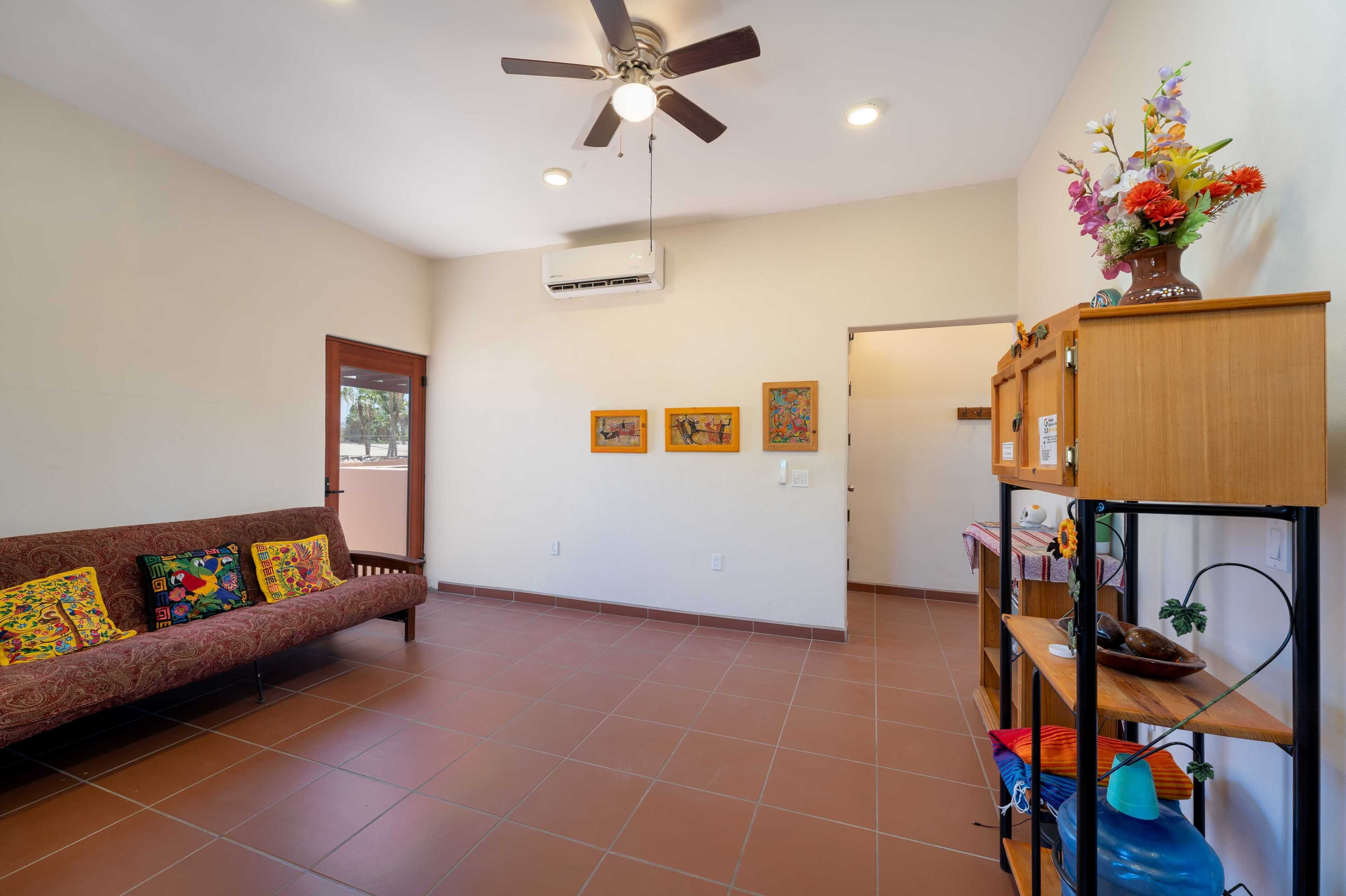 A living room with a sofa, a ceiling fan, and a wall-mounted shelf with decorative items.