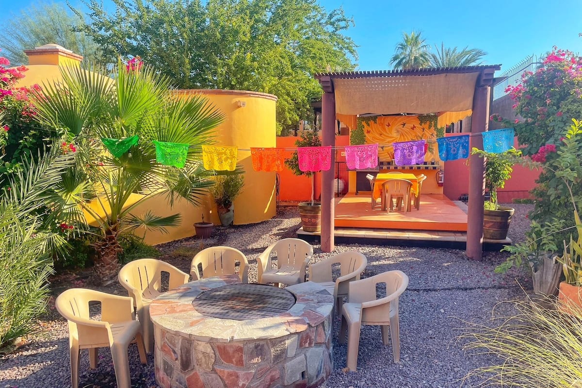 Un patio con un hogar a leña de piedra, sillas de plástico y una mesa.