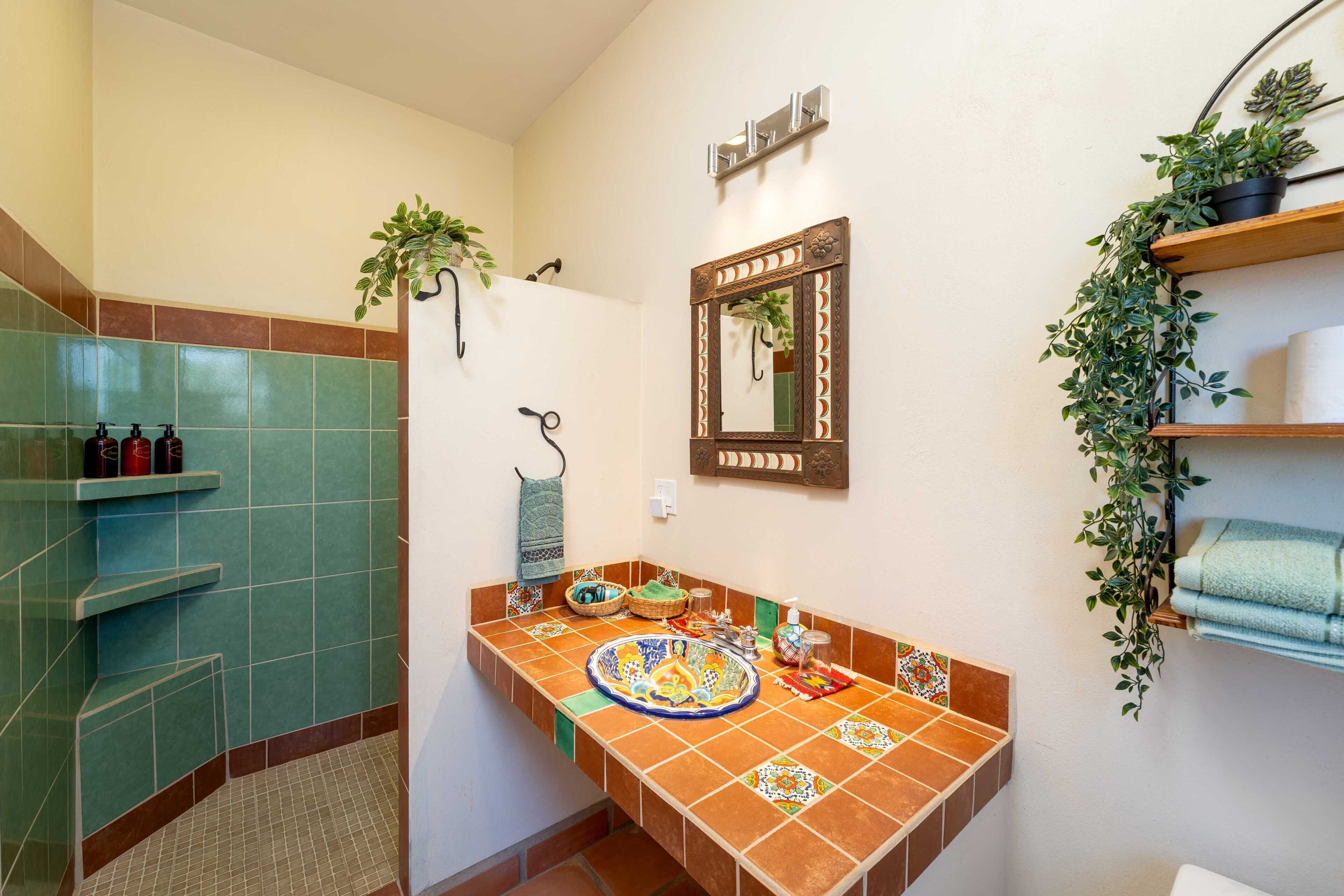 Un baño con piso de baldosas, un lavamanos con detalles de azulejos decorativos, un espejo y un perchero con toallas.