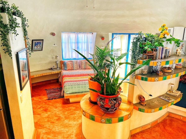A room with a bed, a small desk, a potted plant, and a shelf with books and decorative items. - dome suite domes (Loreto)