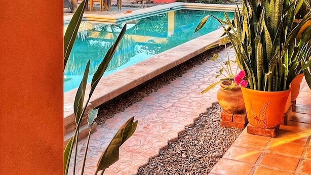 A pool area with a clear view of a yellow building, a thatched-roof structure, and potted plants. - dome suite domes (Loreto)