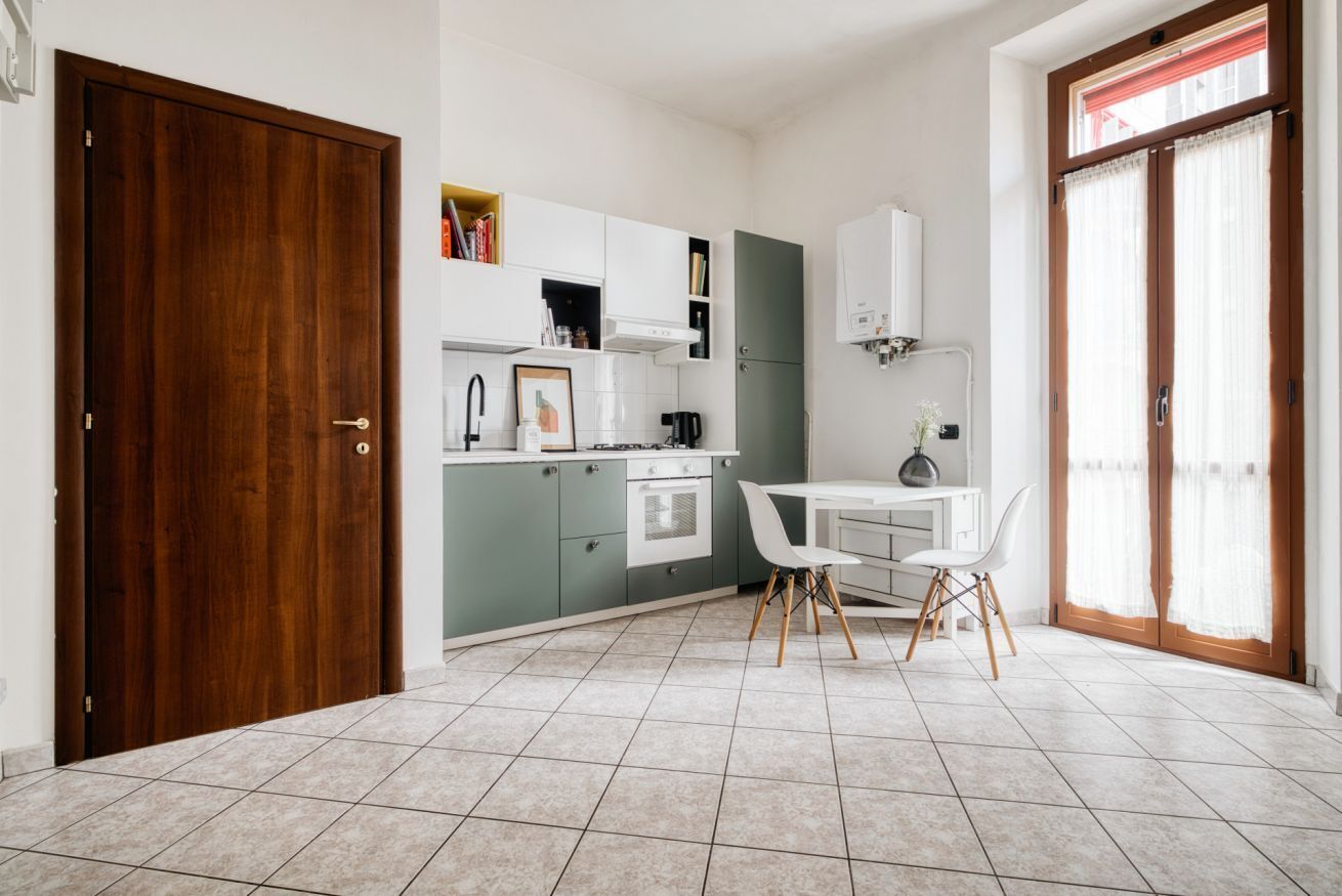 A compact kitchen with a dining area, a wooden door, and a window with curtains.