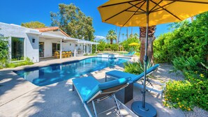 A swimming pool with lounge chairs and an umbrella, surrounded by greenery and a house. - Sun and Games -  - The Ultimate Central Palm Springs Escape! (Palm Springs)