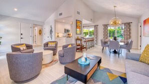 A spacious living area with grey sofas, a coffee table, and a dining area with a chandelier. - Sun and Games -  - The Ultimate Central Palm Springs Escape! (Palm Springs)