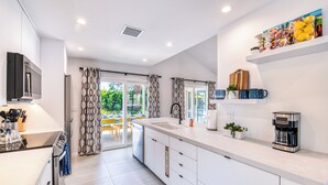 A modern kitchen with a built-in oven, a coffee machine, and a dining area with a table and chairs. - Sun and Games -  - The Ultimate Central Palm Springs Escape! (Palm Springs)