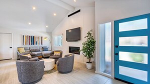 A modern living room with a sofa set, a flat-screen TV, a fireplace, and a large blue door. - Sun and Games -  - The Ultimate Central Palm Springs Escape! (Palm Springs)