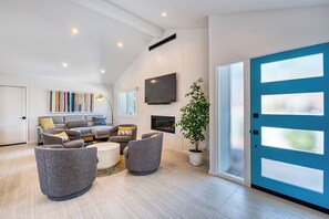 Un salon moderne avec un ensemble de canapés, un téléviseur à écran plat, une cheminée et une grande porte bleue.