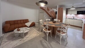 A modern living room with a brown sofa, a round coffee table, and a dining area with white chairs and a wooden table. - Villa Rosa By Avecoeur (Sainte-Maxime)